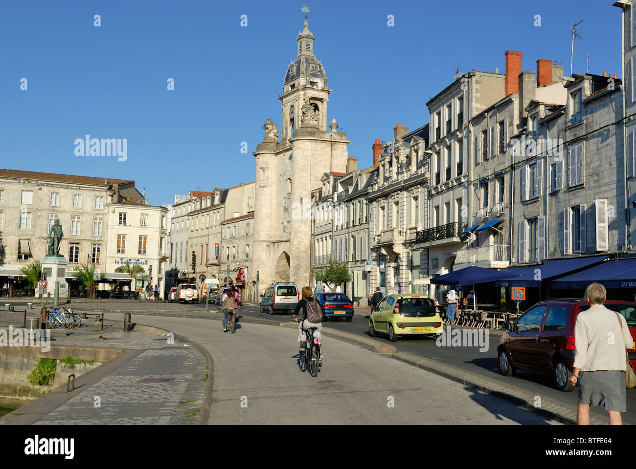 Con la Porte de la Grosse la storica torre dell'orologio in background persone viaggi Quai Valin, la strada principale di La Rochelle, Francia. Foto Stock