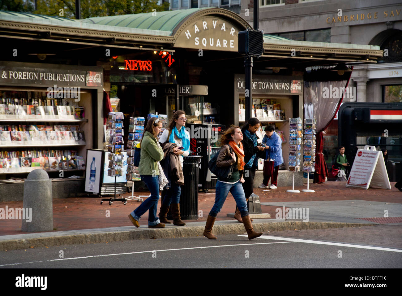 Gli studenti cross Massachusetts Avenue in Harvard Square, Cambridge, MA. Sullo sfondo è la notizia di stand e la stazione della metropolitana. Foto Stock