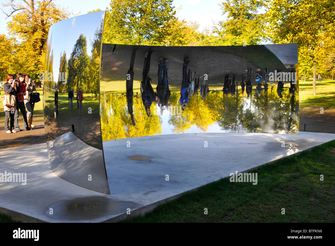 I visitatori di colori autunnali a Kensington Gardens che guardano immagini riflesse di se stessi in uno degli specchi Anish Kapoor Sky C Curve Londra Inghilterra Regno Unito Foto Stock