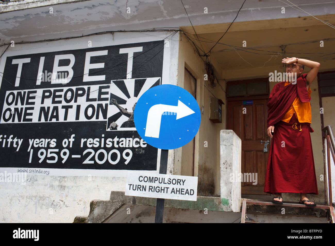Un Buddista monaco tibetano in piedi da un 'Free Tibet " murale in stile McLeod Ganj, India Foto Stock