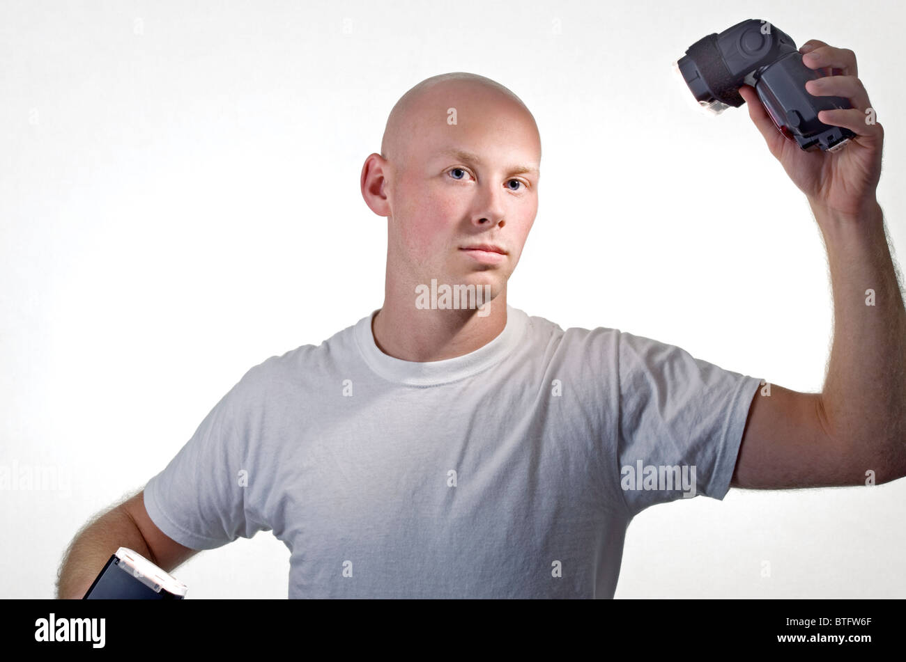 Uomo calvo (20-25) in un bianco tee shirt e sfondo bianco e di contenimento essendo illuminata da due telecamere wireless lampeggia. Foto Stock