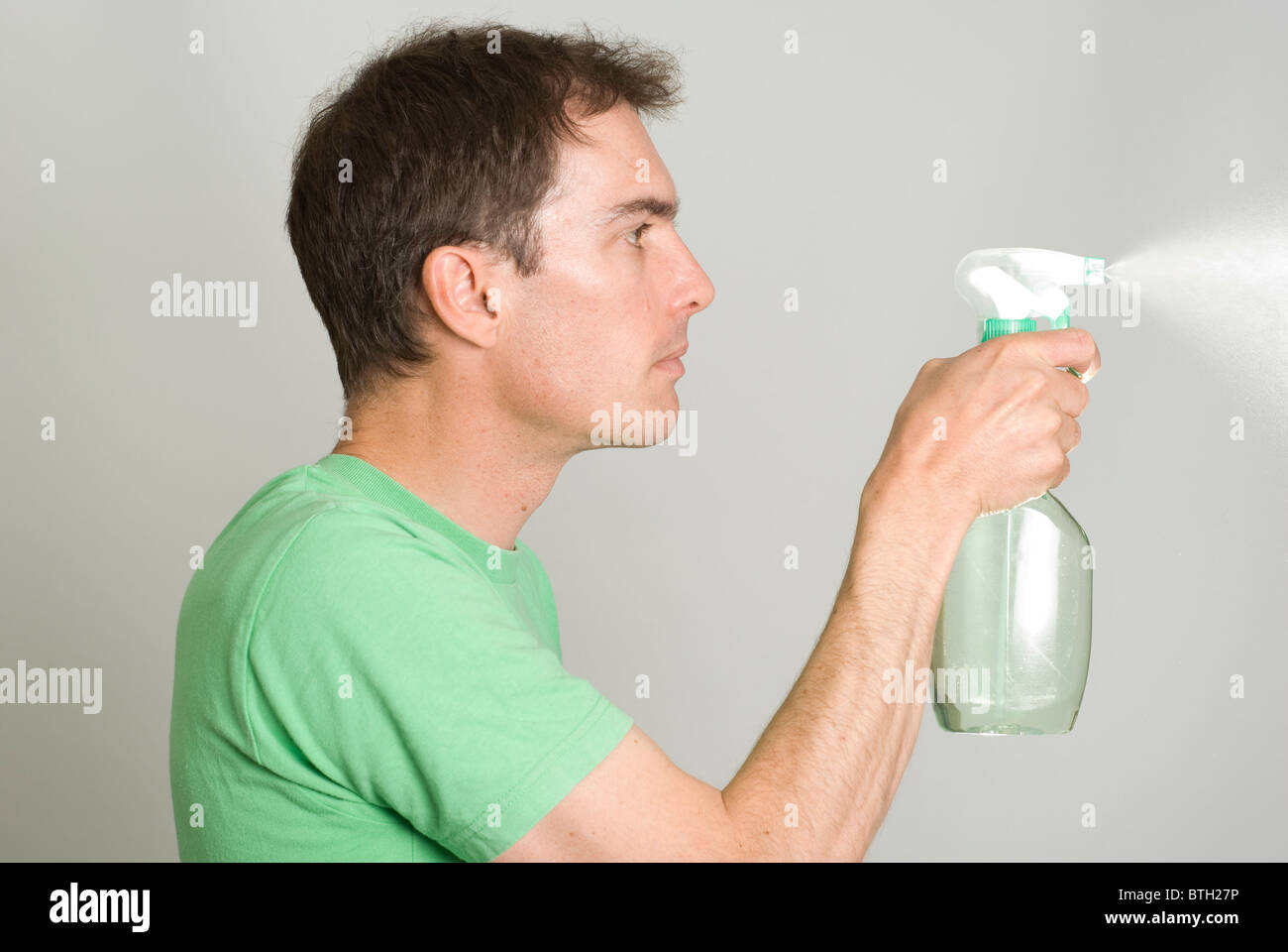 Vista laterale dell'uomo utilizzando la bottiglia spray spruzzare una nebulizzazione di liquido. Foto Stock