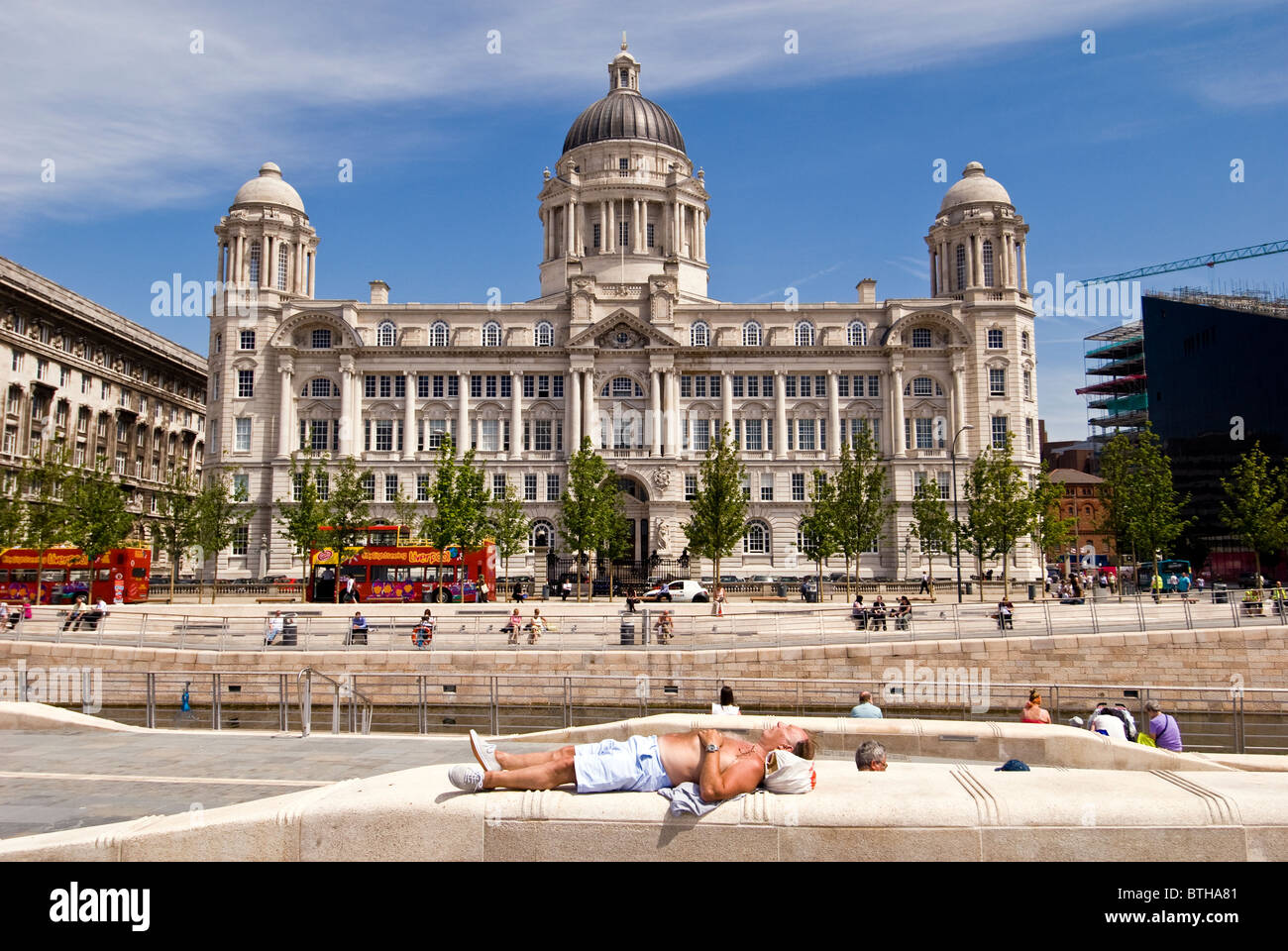 L'uomo la posa sul banco a prendere il sole di fronte del porto di Liverpool edificio, England, Regno Unito Foto Stock