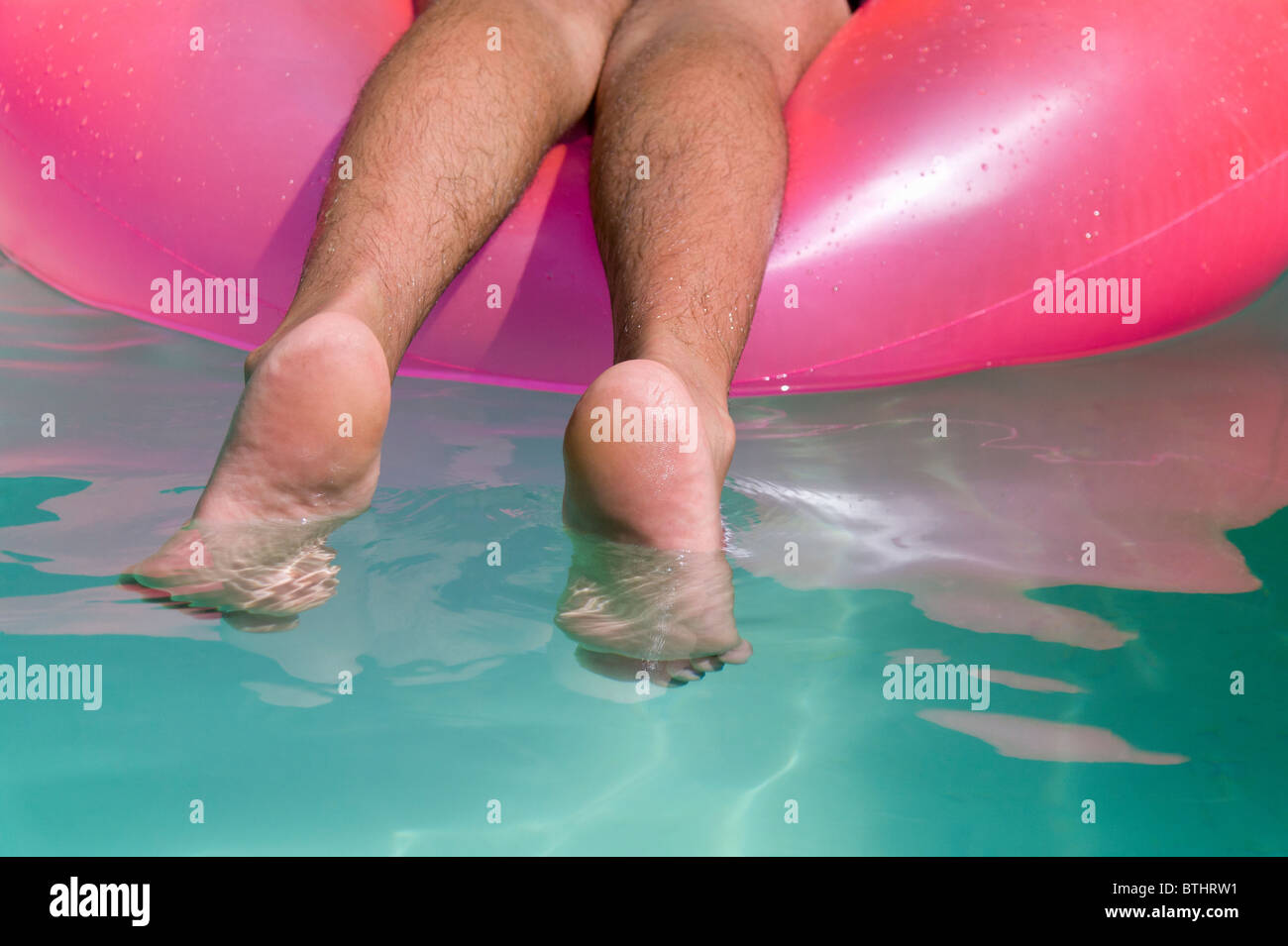 L uomo a prendere il sole sul Rosa Lilo gonfiabile in piscina Foto Stock