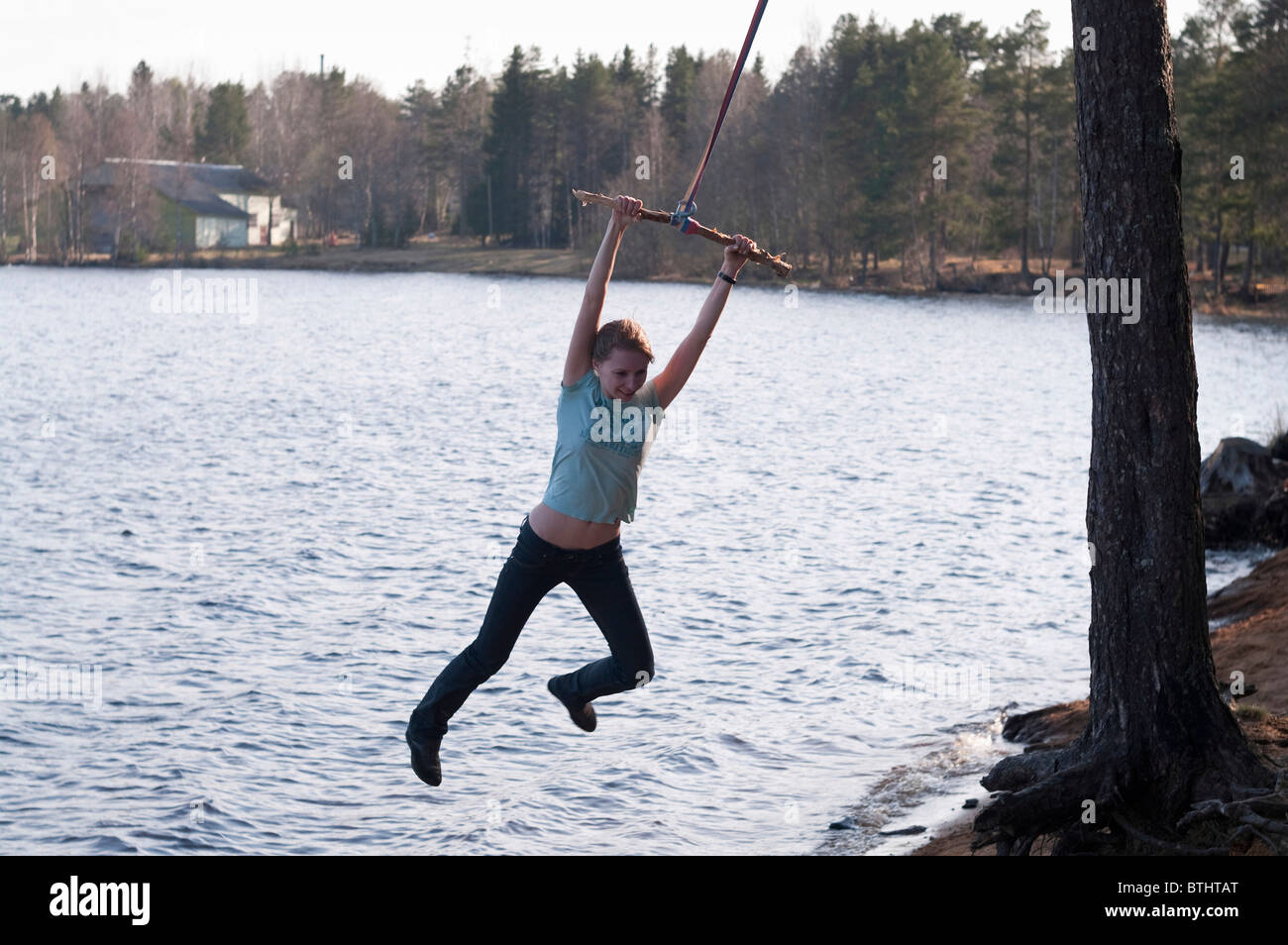 Ragazza giovane oscillare sul bungee attorno all'albero in riva al lago Foto Stock