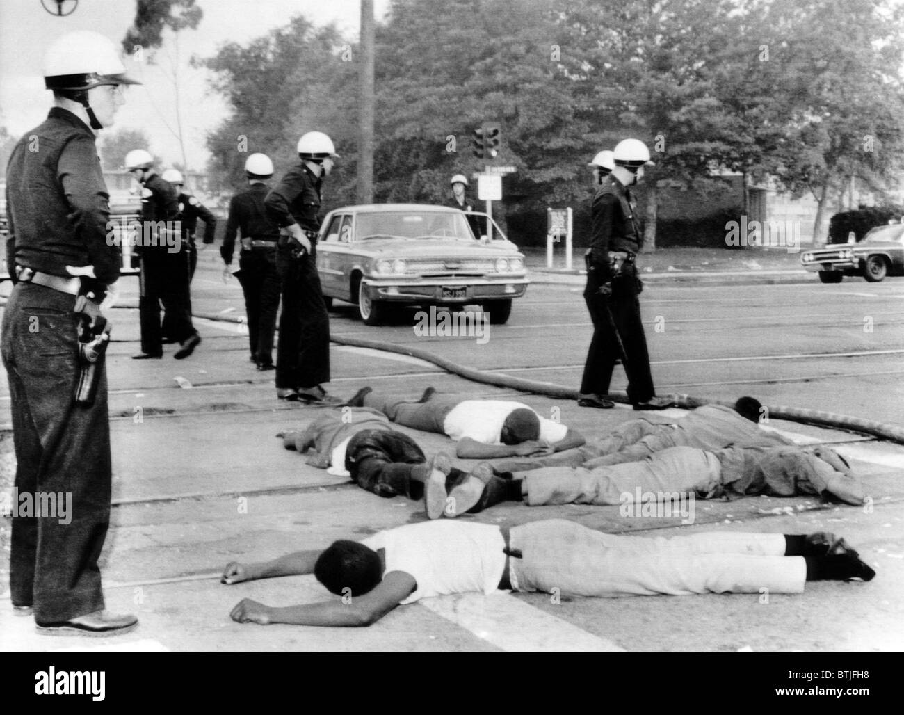 Gli ufficiali di polizia stand su sospetti di saccheggiatori durante il quarto giorno di scontri in watt, California, 1965. La cortesia: Archivi CSU/E Foto Stock