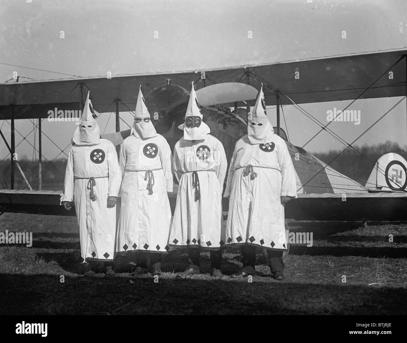 Quattro incappucciati del Ku Klux Klan membri pongono in da del loro aeroplano che porta una croce uncinata emblema. 1922 foto. Foto Stock