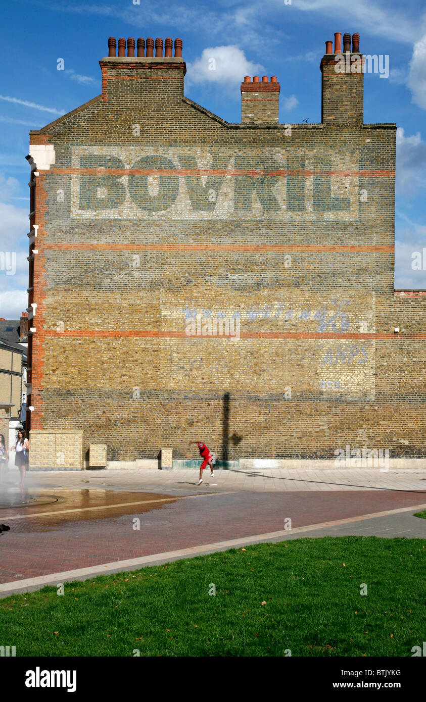 Piccolo Ragazzo di gettare una sfera contro la 'Bovril' sulla parete Windrush Square, Brixton, London, Regno Unito Foto Stock