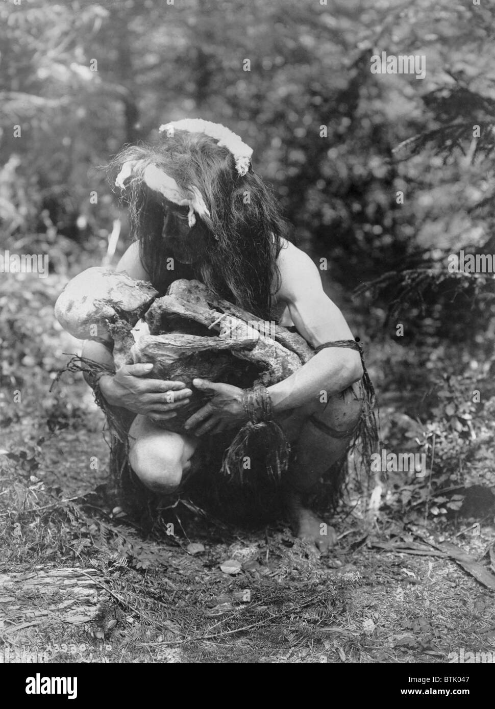 Il Kwakiutl uomo, accovacciata, cullano mummia legato in posizione fetale, titolo: preparare da mangiare la mummia", fotografia di Edward S. Curtis, circa 1911. Foto Stock
