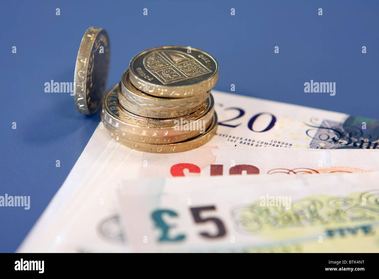 Una pila di sterling £2 e £1 monete su una pila di £ 5, £10, £20 note con un allentamento £1 gettone sulla sua estremità Foto Stock