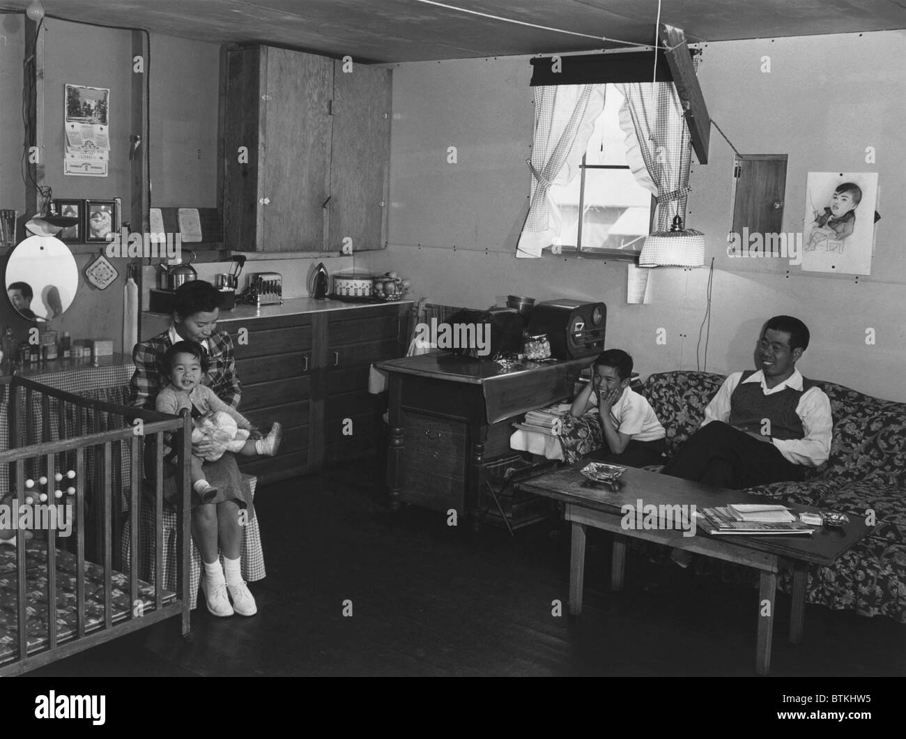 Giapponese famiglia americana internati a Manzanar Relocation Center durante la Seconda Guerra Mondiale. Il sig. e la Sig.ra Richard Izuno e i loro due bambini pongono una sola camera (ca. 20' x20') caserma home. 1943 fotografia di Ansel Adams. Foto Stock