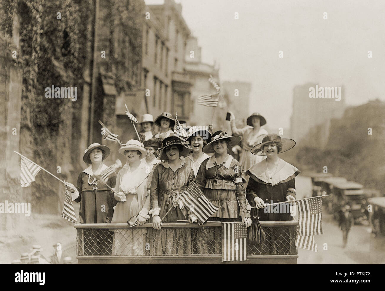 Sorridente giovani donne sventolando bandiere dalla cima di un veicolo aperto in una New York City parade. Ca. 1910-1915. Foto Stock