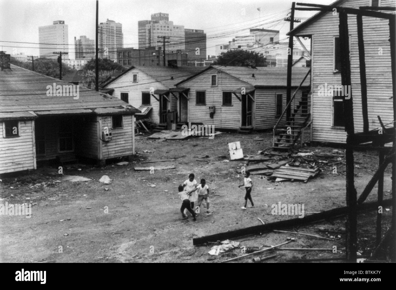 Americano africano di bambini che giocano in baraccopoli in vista di edifici alti in background. North Carolina, ca. 1966. Foto Stock