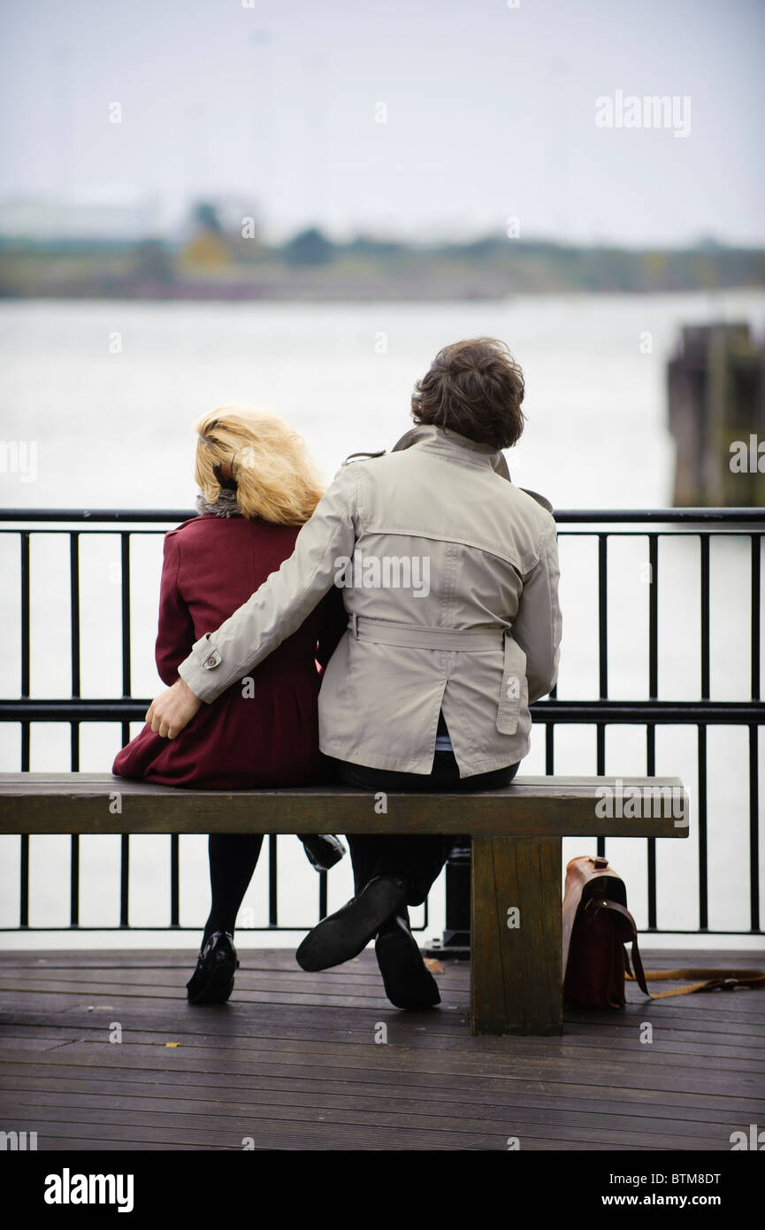 Vista posteriore di una giovane coppia seduta su una panchina per la Baia di Cardiff Wales UK Foto Stock