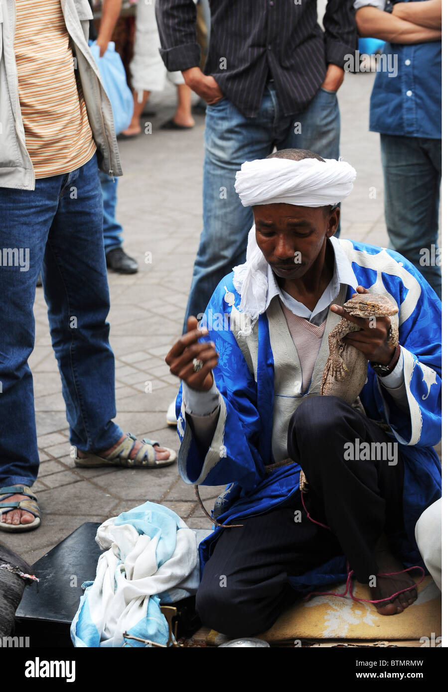 Uomo Turbaned spiegando le proprietà curative di un Live Iguana ad una cerchia di persone in Djemaa el Fna a Marrakech. Foto Stock