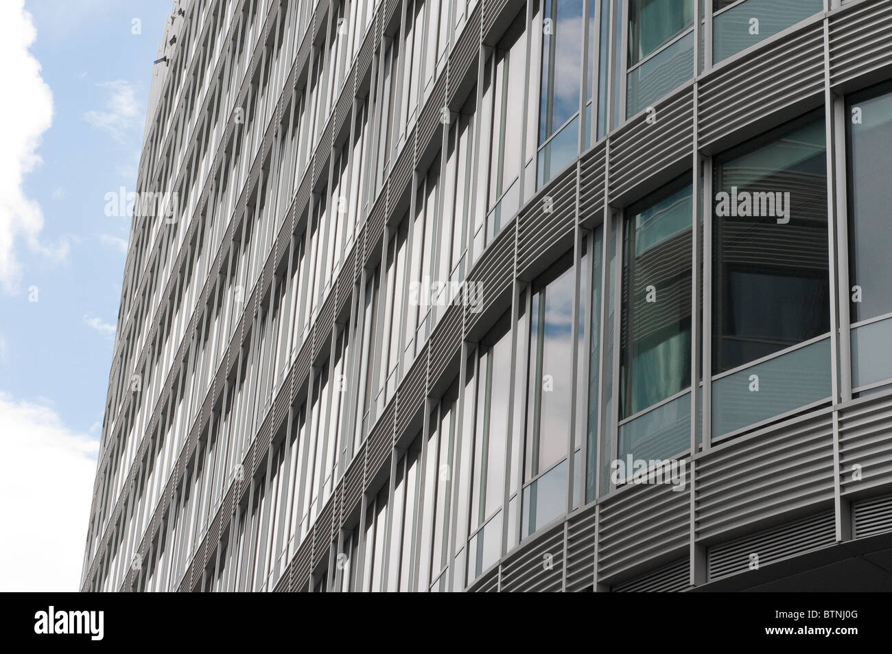 Vista della curva esterna edificio per uffici a guardare in alto verso il blu e il cielo nuvoloso Foto Stock