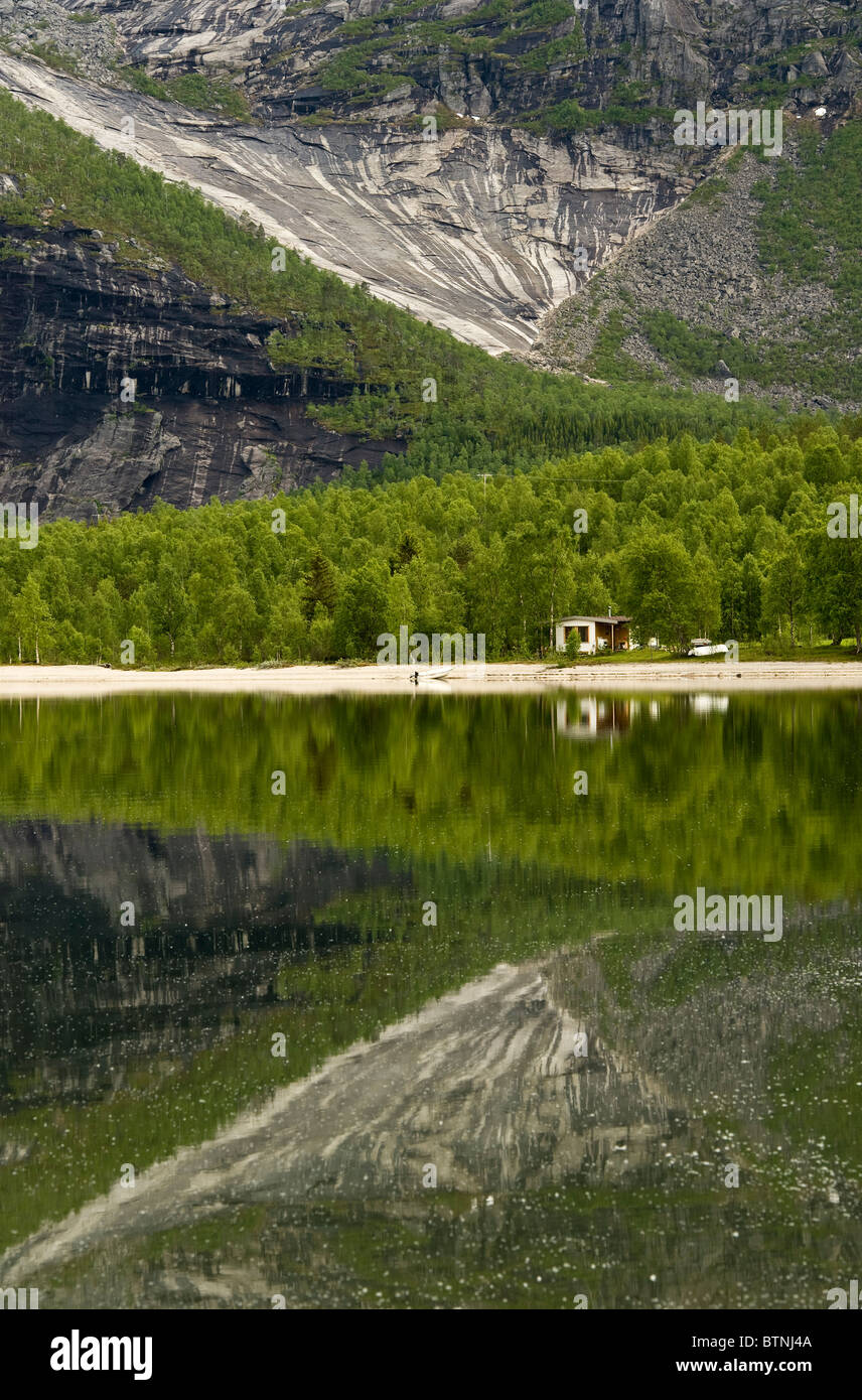 Cabina con spiaggia. La riflessione di montagna e gli alberi ancora la superficie dell'acqua. Nordland, nel nord della Norvegia Foto Stock