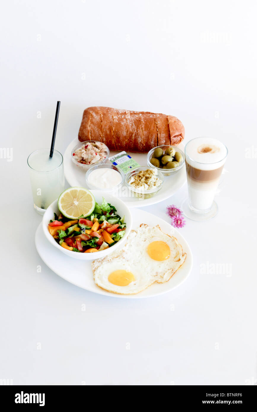 Tradizionale colazione israeliana con due uova fritte, formaggio giallo, insalata, un rotolo di fresco e una tazza di cappuccino Foto Stock
