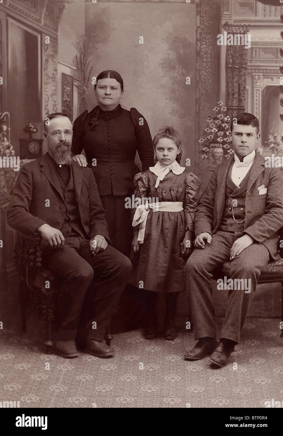 1890 foto vintage famiglia in un formale studio shot.Questa fotografia è ingiallito con l'età. Seduto è padre e figlio con la madre e la figlia in piedi Foto Stock