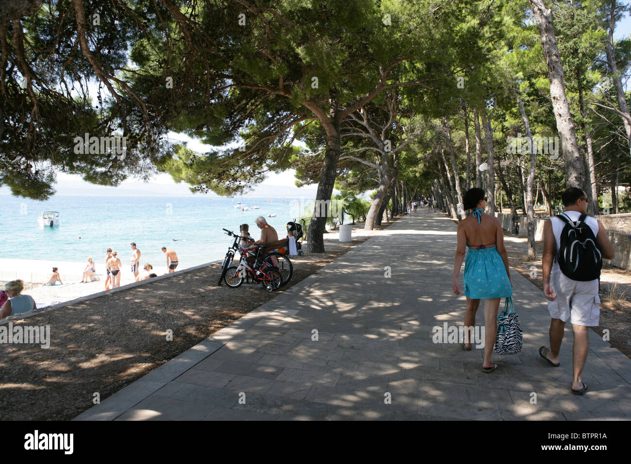 La gente a piedi lungo il viale ombreggiato vicino alla spiaggia di Bol sulla isola di Brac, Croazia Foto Stock