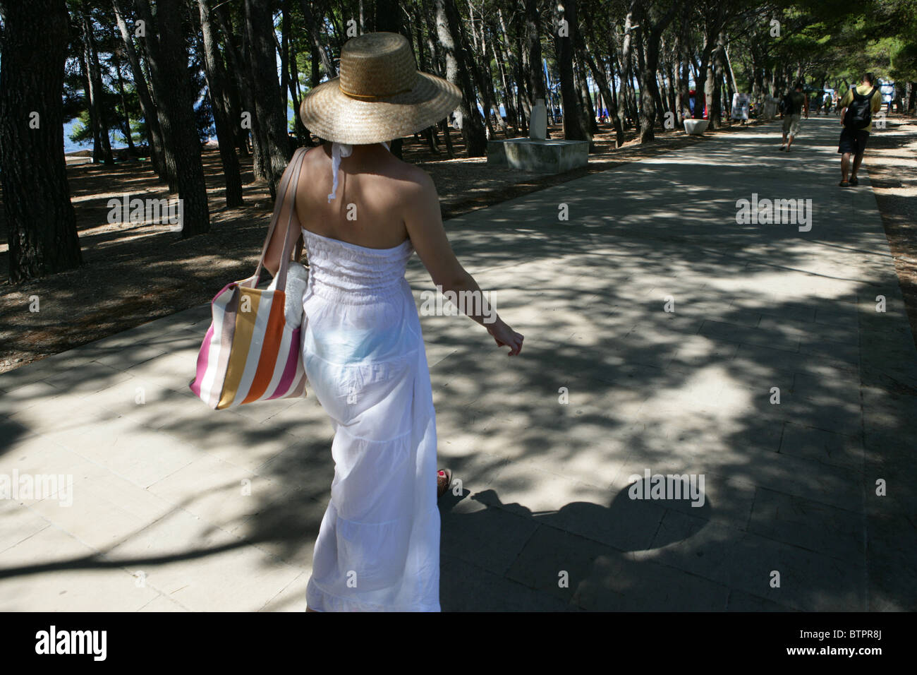 Una giovane donna cammina lungo il viale ombreggiato vicino alla spiaggia di Bol sulla isola di Brac, Croazia Foto Stock