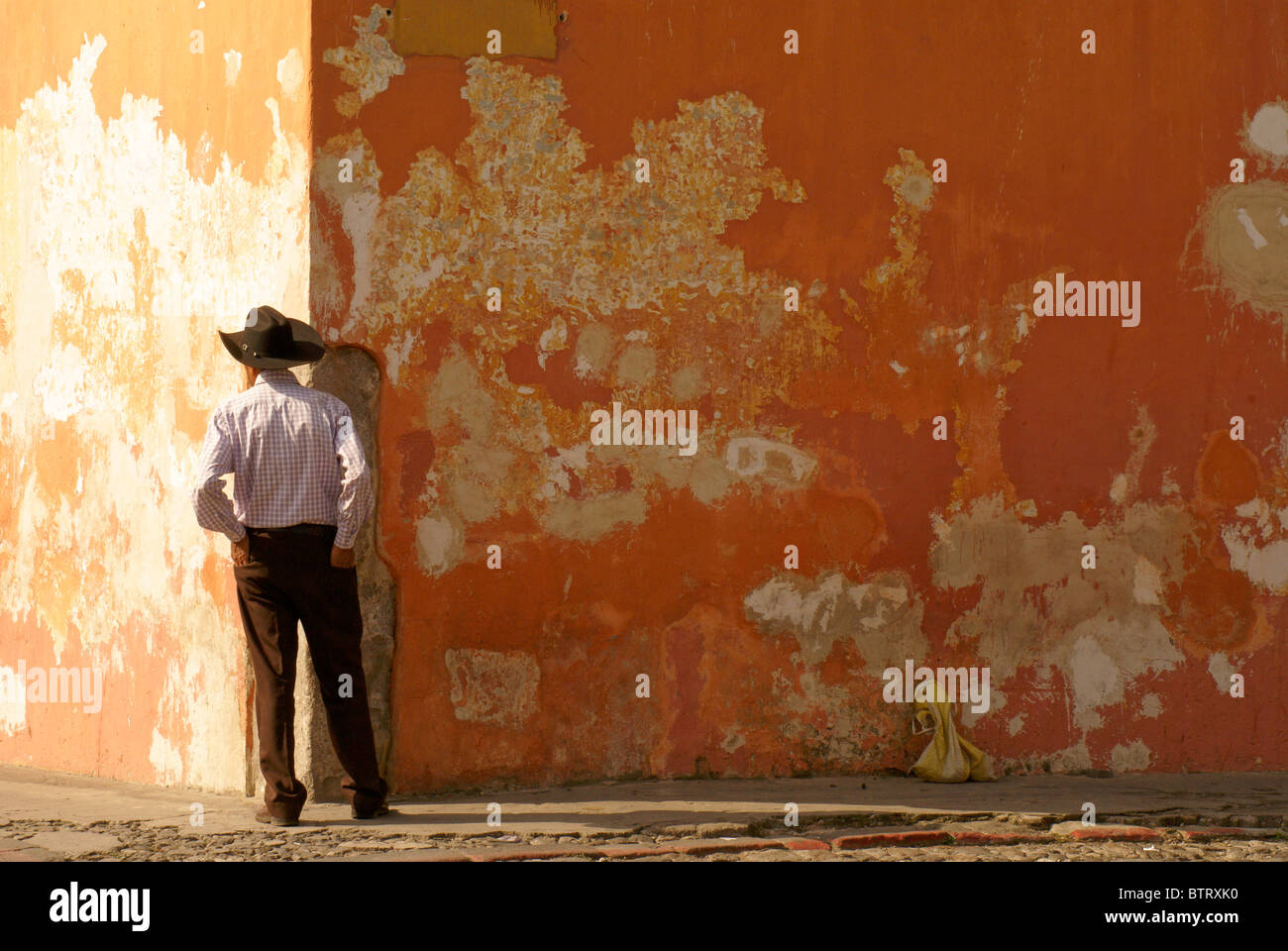 Uomo in piedi di fronte ad una parete colorata in Antigua, Guatemala. Antigua è un sito patrimonio mondiale dell'UNESCO. Foto Stock