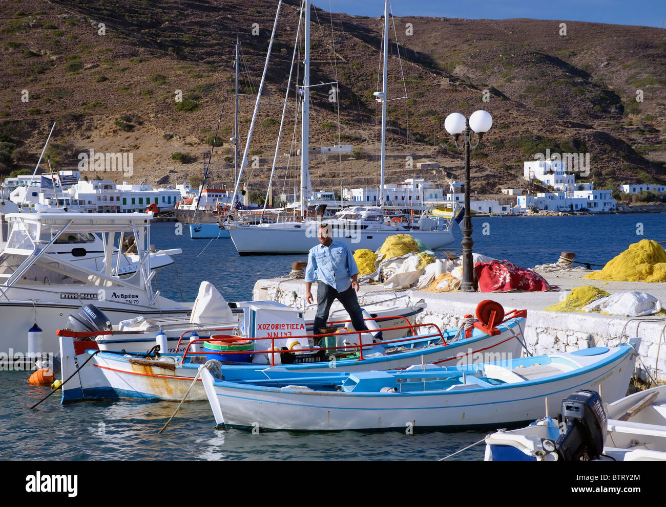 Pescatore greco in piedi su una piccola barca ormeggiata nel porto di Xilokeratidi, su la più orientale Cyclade isola di Amorgos. Foto Stock
