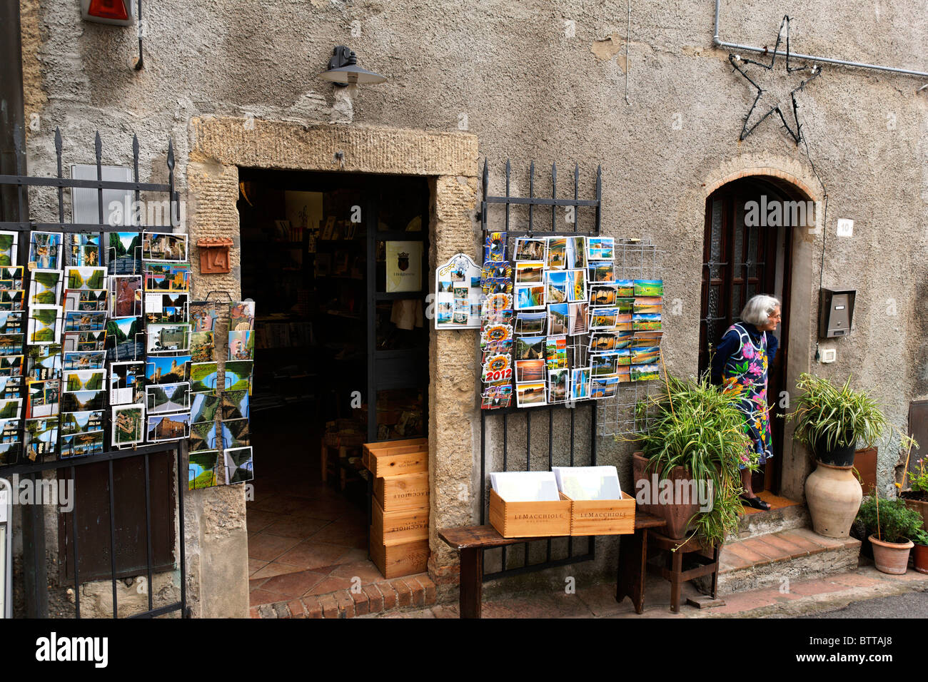 Cartoline colorate al di fuori di un negozio di Bolgheri e la vecchia donna lookimg fuori la sua porta,Toscana, Italia Foto Stock