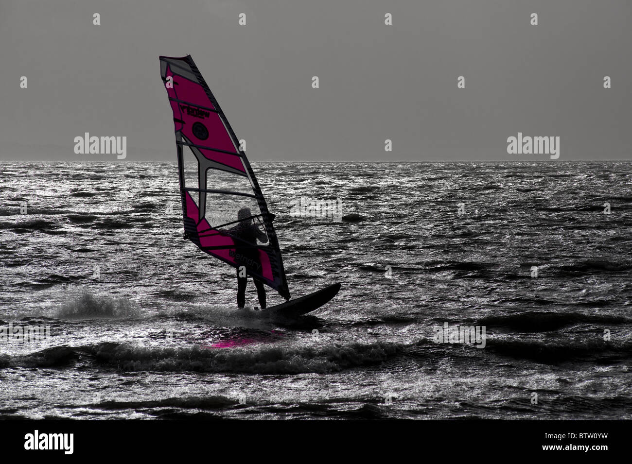 Lone windsurf stagliano contro il cielo grigio con il colore della vela enhanced. Foto Stock