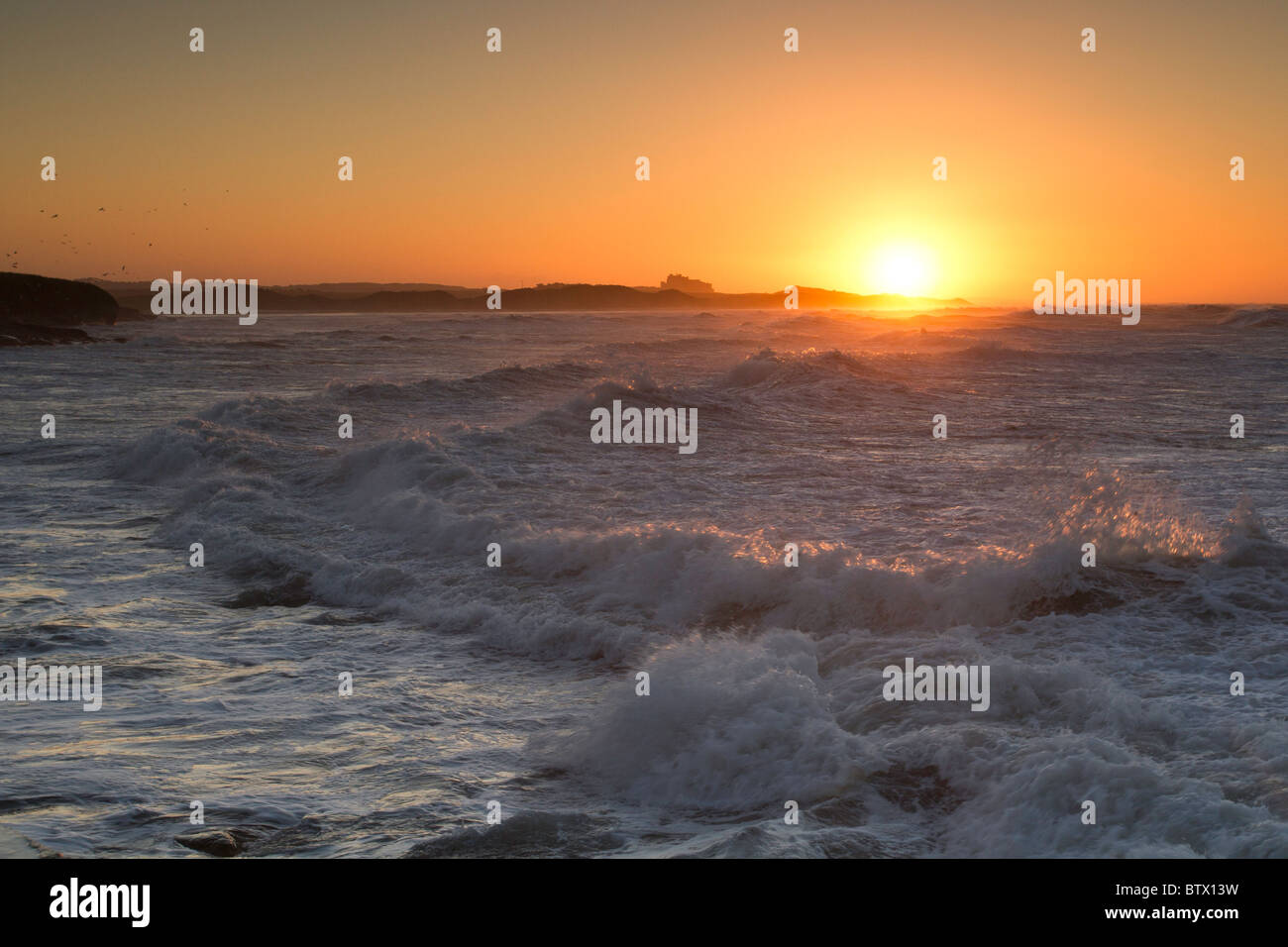 Tramonto sul castello di Bamburgh da Seahouses Foto Stock