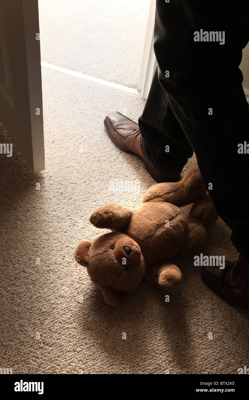 Uomo di gambe e feett passato a passo di un bambino orsacchiotto sul pavimento per lasciare la camera. Foto Stock