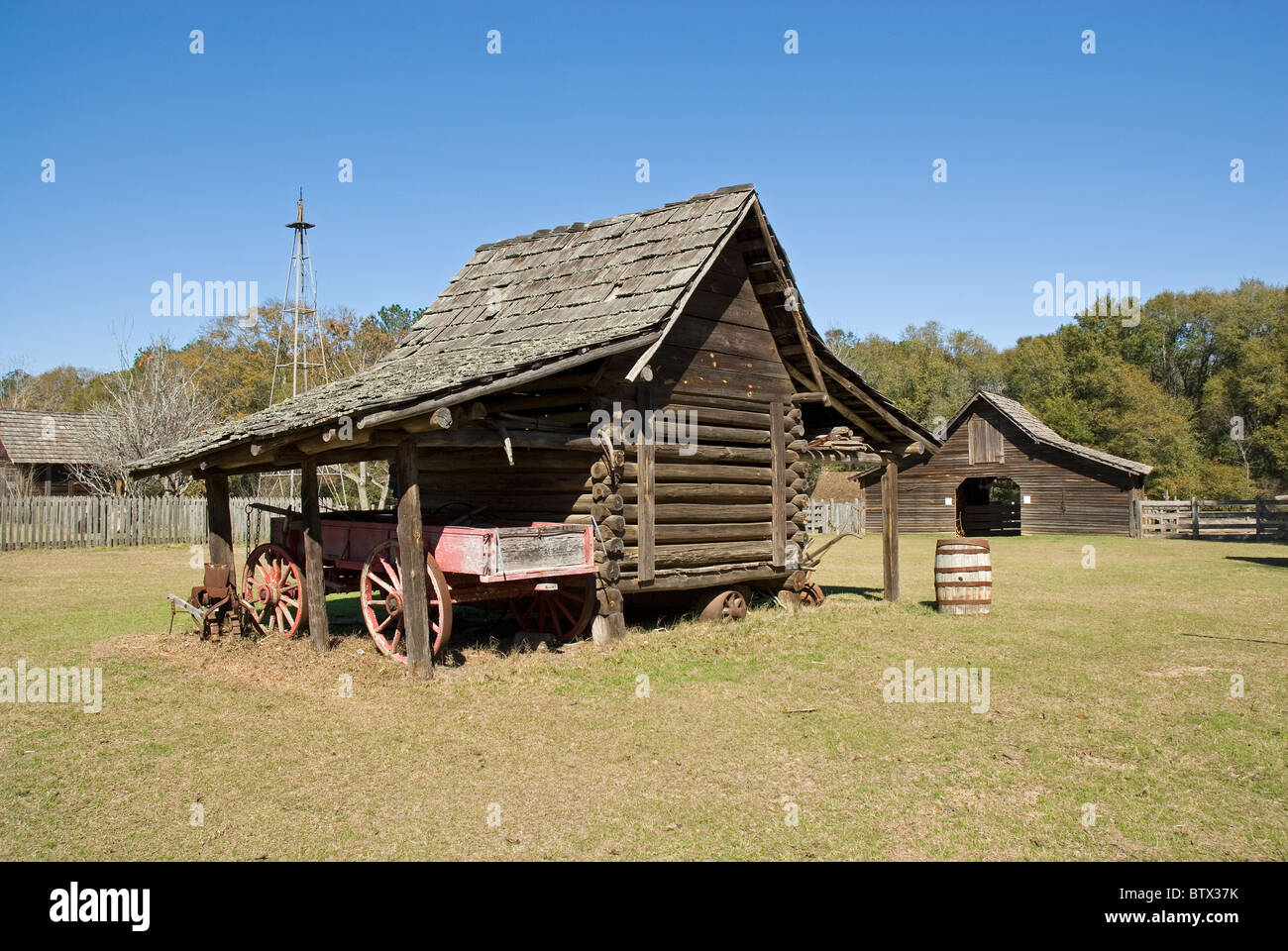 Un log cabin tipo capannone per il rimessaggio di un vecchio carro seduto accanto a esso. Vi è un vecchio fienile in background. Foto Stock