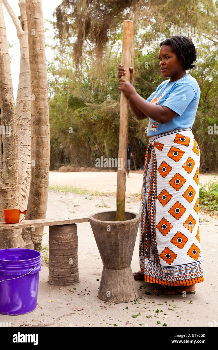 Tradizionale preparazione di cibo africano come una donna tanzaniana sterza ingredienti utilizzando un grande pestello di legno e mortaio di pietra, Dar es Salaam, Tanzania Foto Stock