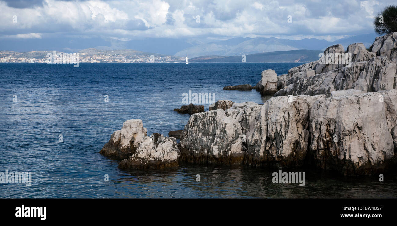 Lontane vele Yacht da coste rocciose Foto Stock