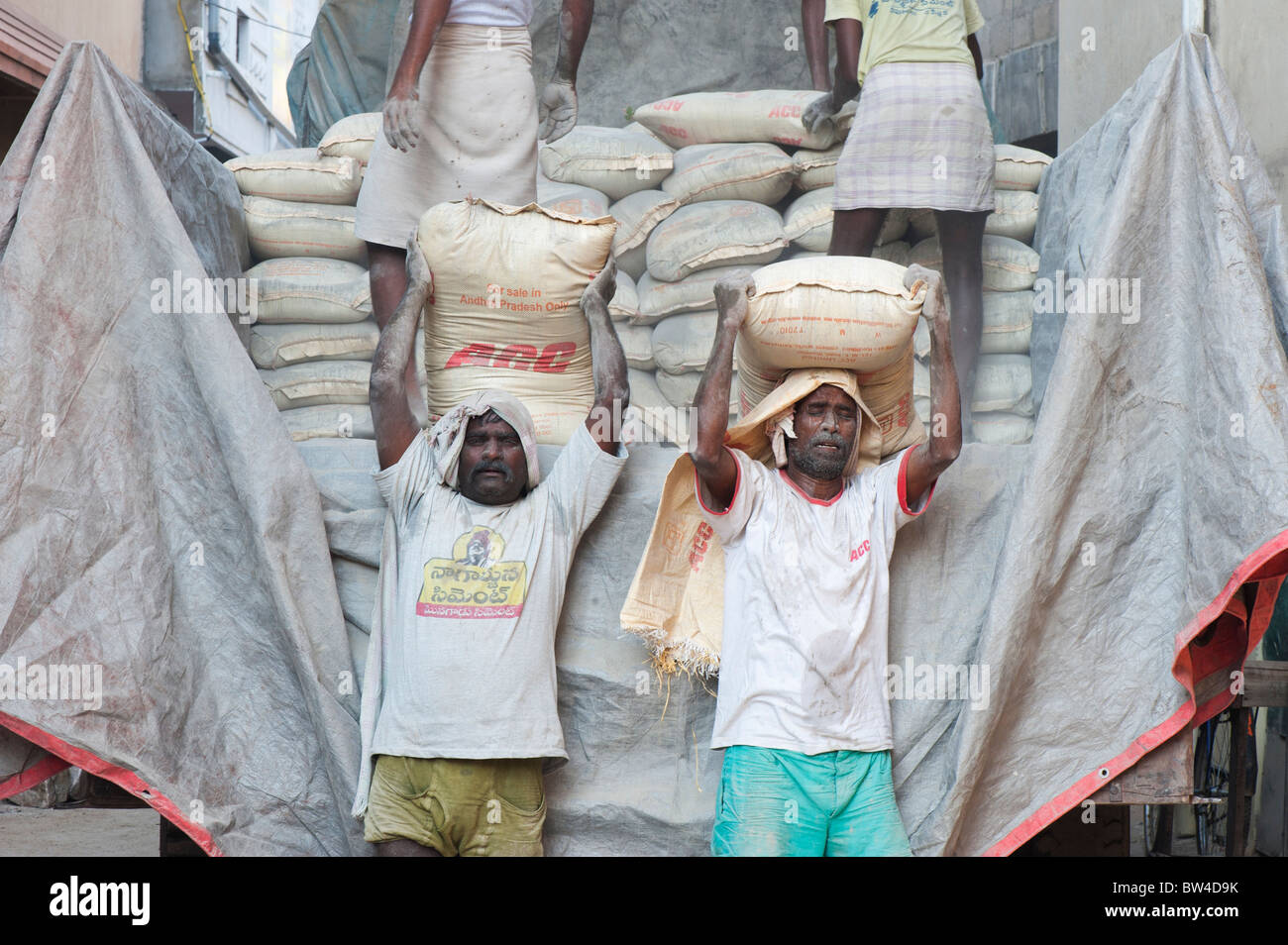 Indian uomini offloading sacchi di cemento da un camion alla costruzione dell'edificio sito. Andhra Pradesh, India Foto Stock