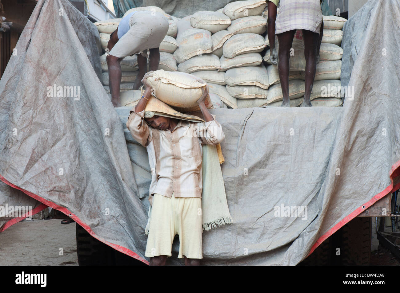 Indian uomini offloading sacchi di cemento da un camion alla costruzione dell'edificio sito. Andhra Pradesh, India Foto Stock