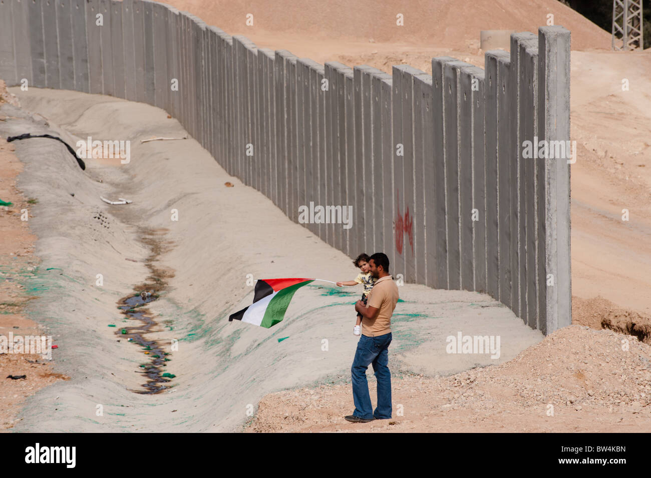 Padre e figlia sventola una bandiera palestinese sostare vicino israeliano barriera di separazione essendo costruito in Cisgiordania. Foto Stock