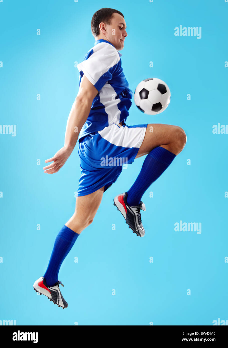 Ritratto di giocatore di calcio jumping con sfera su uno sfondo blu Foto Stock Ritratto di giocatore di calcio jumping con sfera su uno sfondo blu Foto Stock