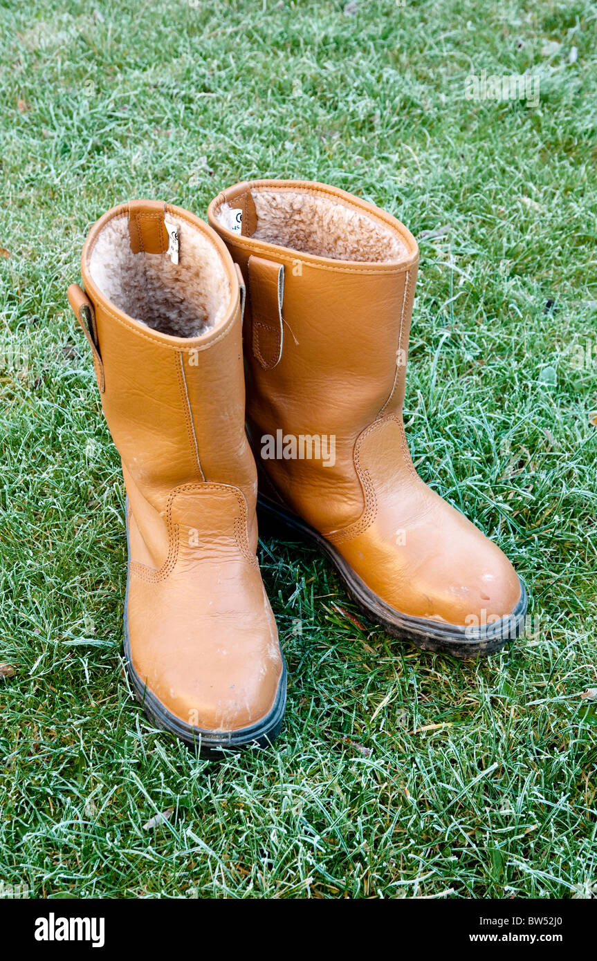 Costruttori stivali - come raccomandato per la salute & sicurezza / protezione requisito - con il pupazzo di neve erba come sfondo. Foto Stock