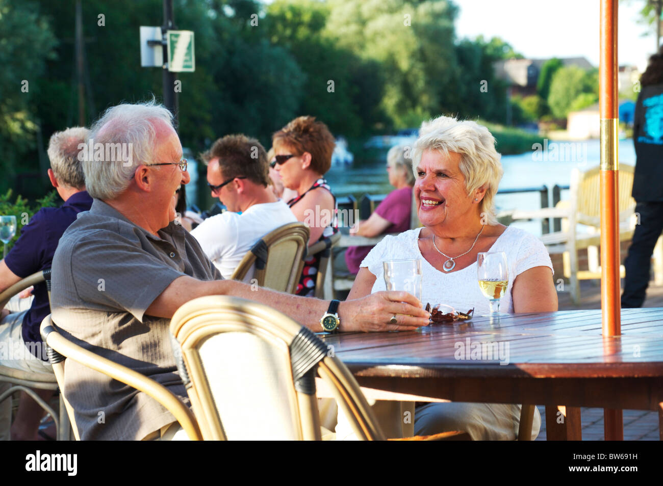 Bianco maturo giovane seduto sul bordo del Norfolk Broads gustando un drink su una sera d'estate Foto Stock