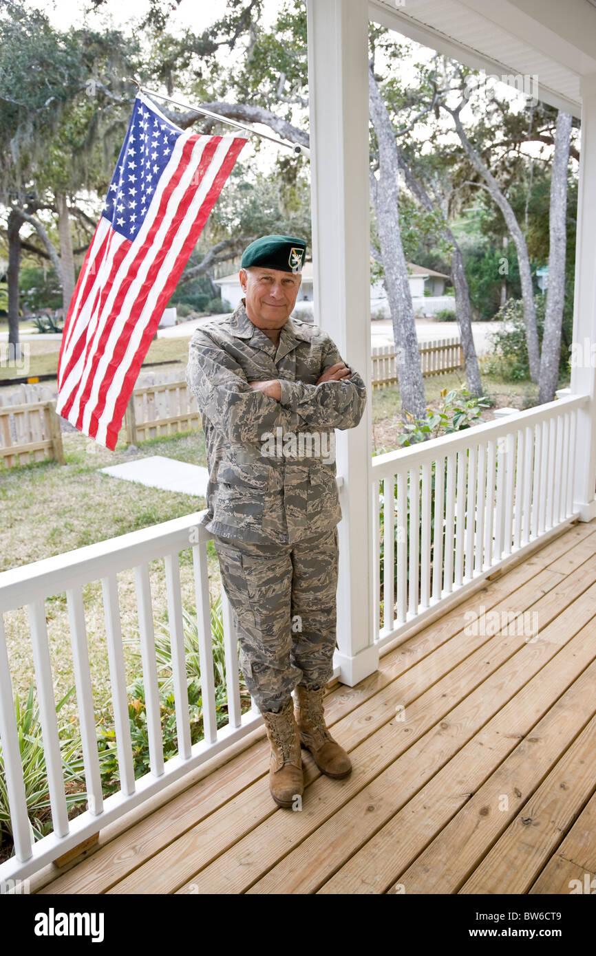 Senior uomo in uniforme militare in piedi dalla bandiera americana sul portico Foto Stock