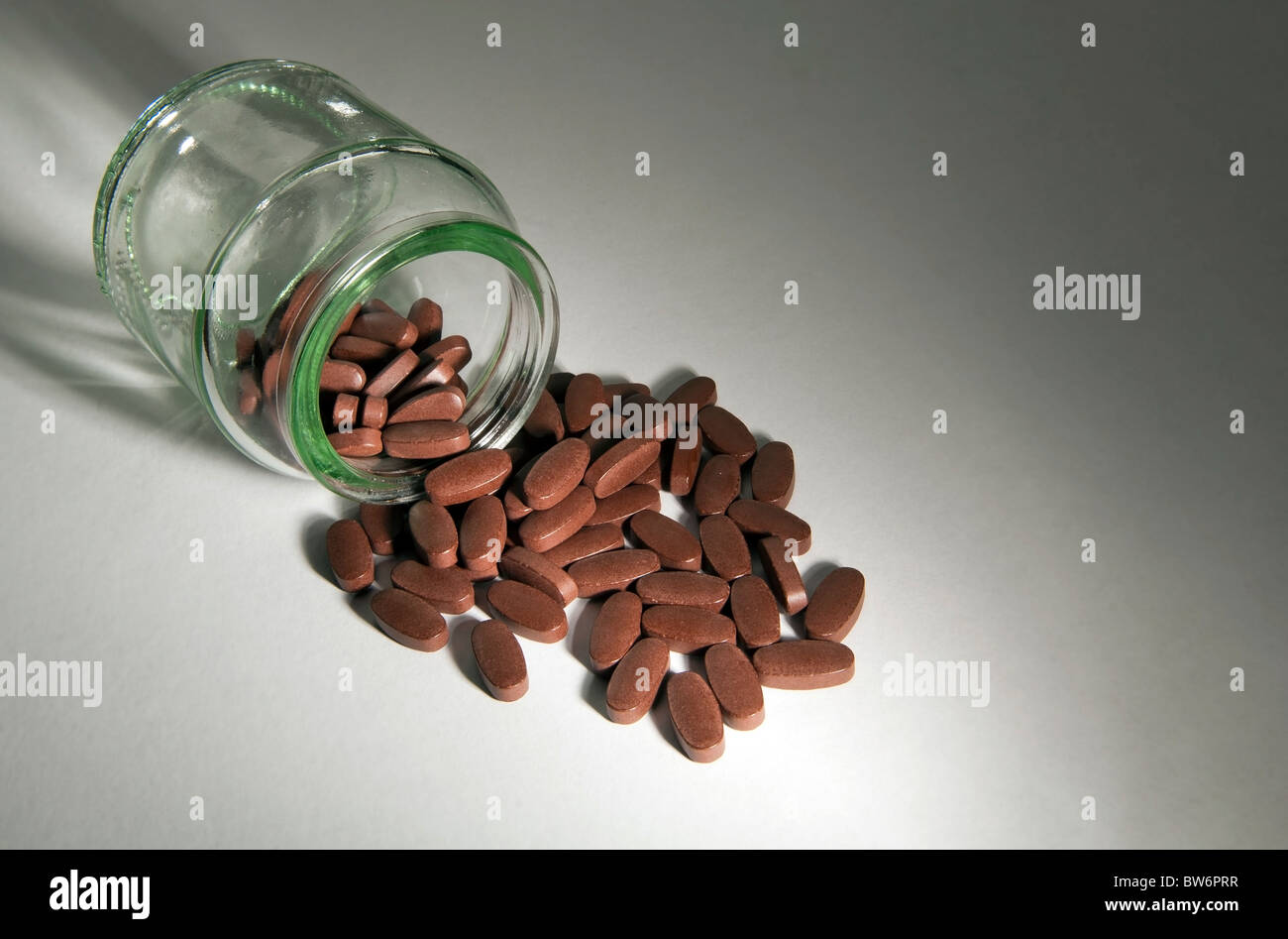 Le pillole generiche fuoriuscita di una bottiglia di vetro chiaro Foto Stock