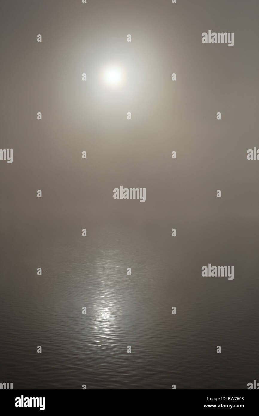Il sole che riflette su un lago nebbioso Foto Stock