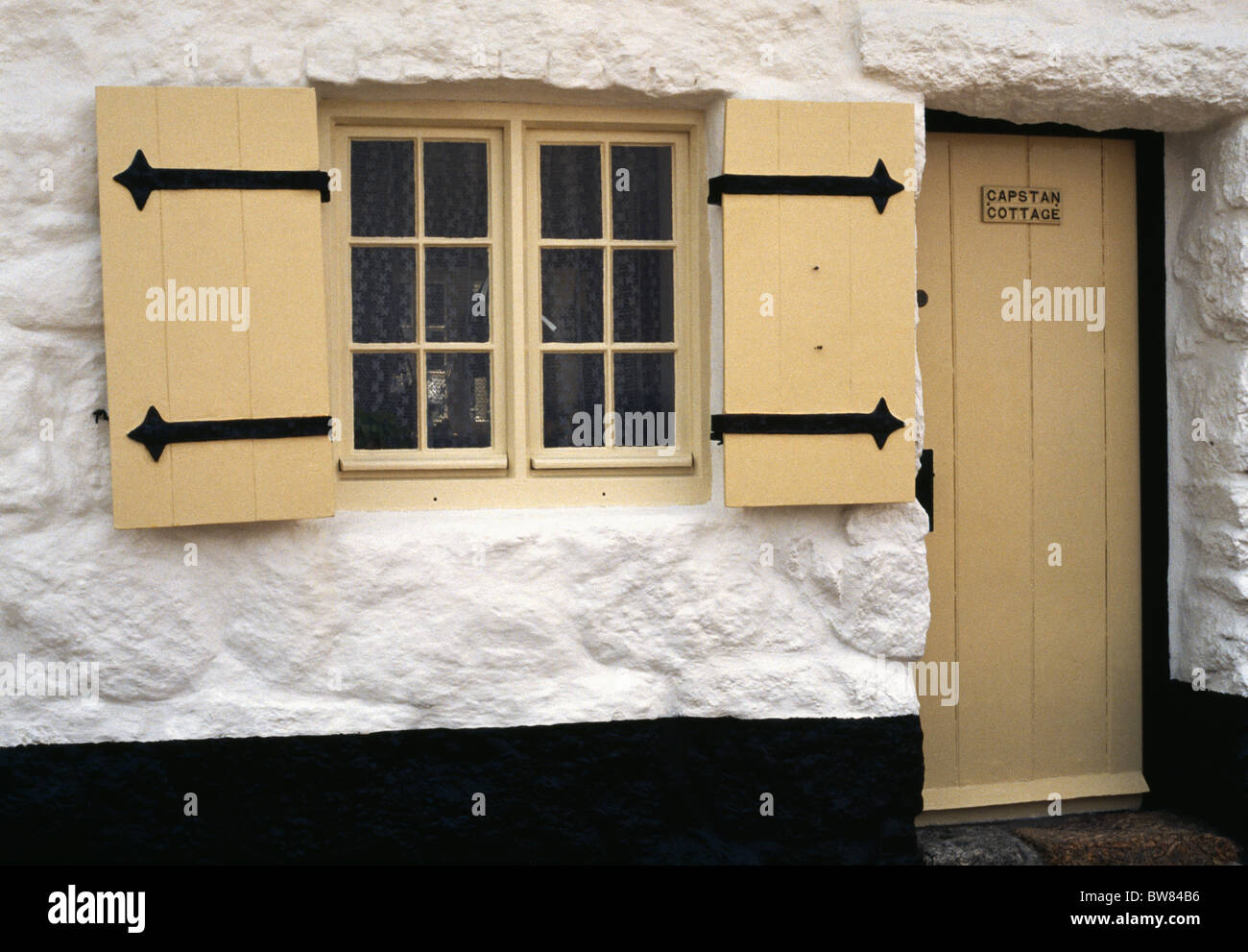 Giallo pallido persiane e porta sul dipinto di bianco cottage in pietra Foto Stock