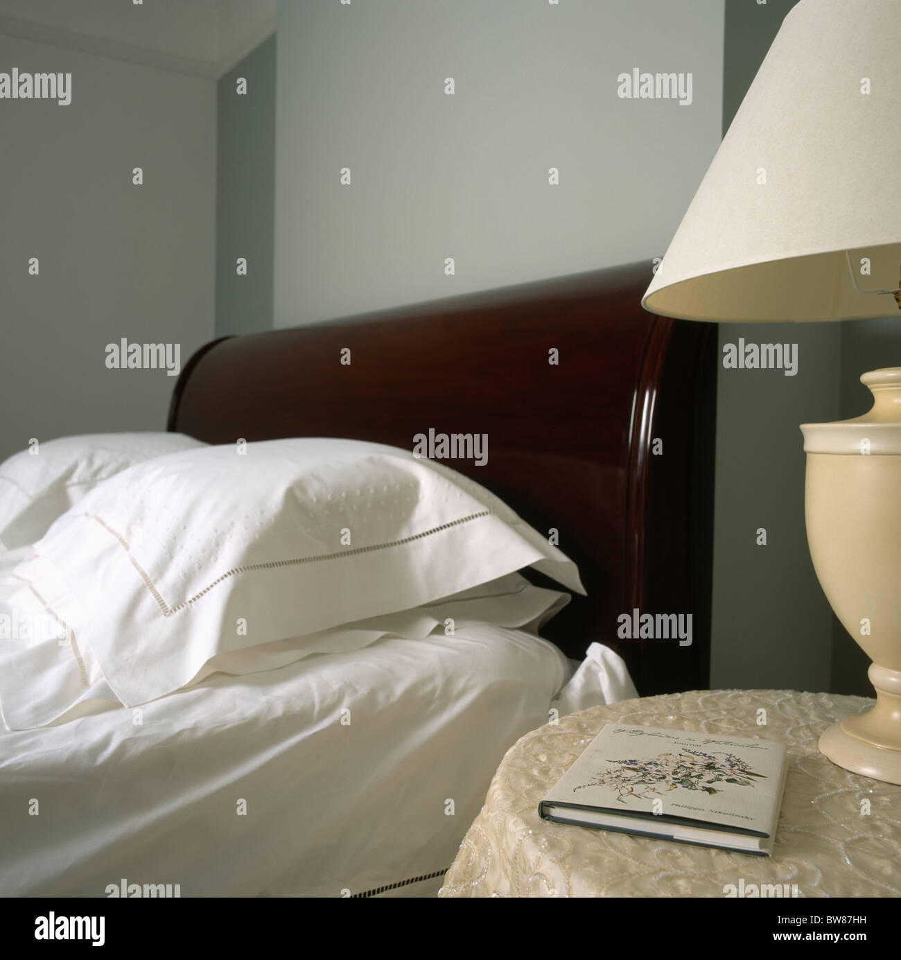 Close-up di sleigh-letto con cotone bianco i cuscini e le lenzuola e il comodino con piccolo libro Foto Stock