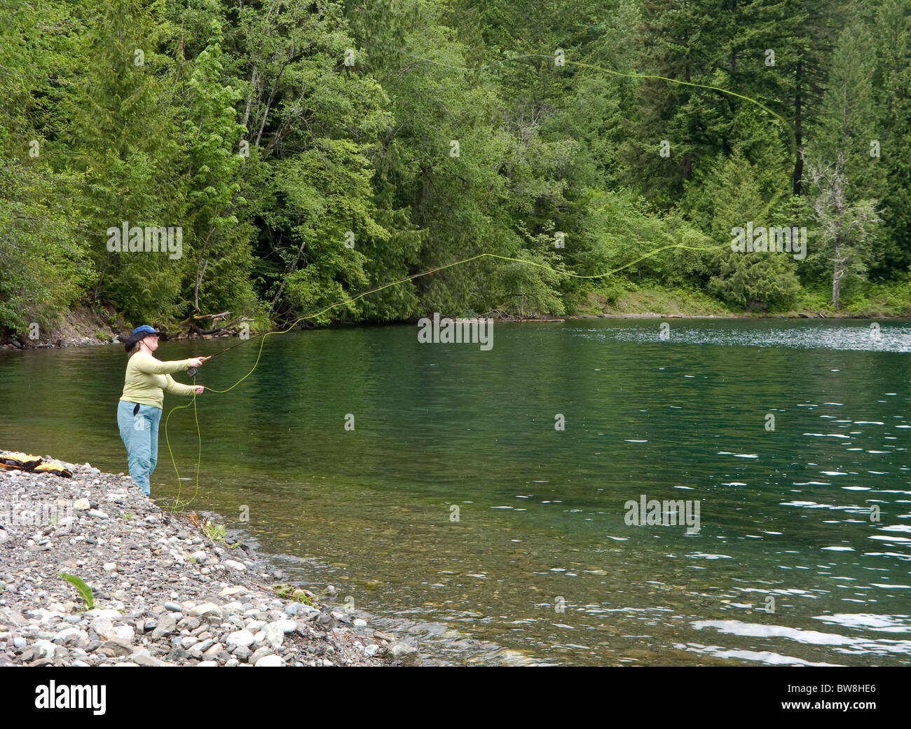 Una donna sola getta un fly line out in acqua lungo le rive di un lago Foto Stock