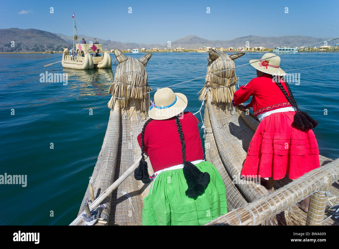 Le donne indigene in costume reed a remi barca sul Lago Titcaca, Uros Isola, Puno, Perù Foto Stock