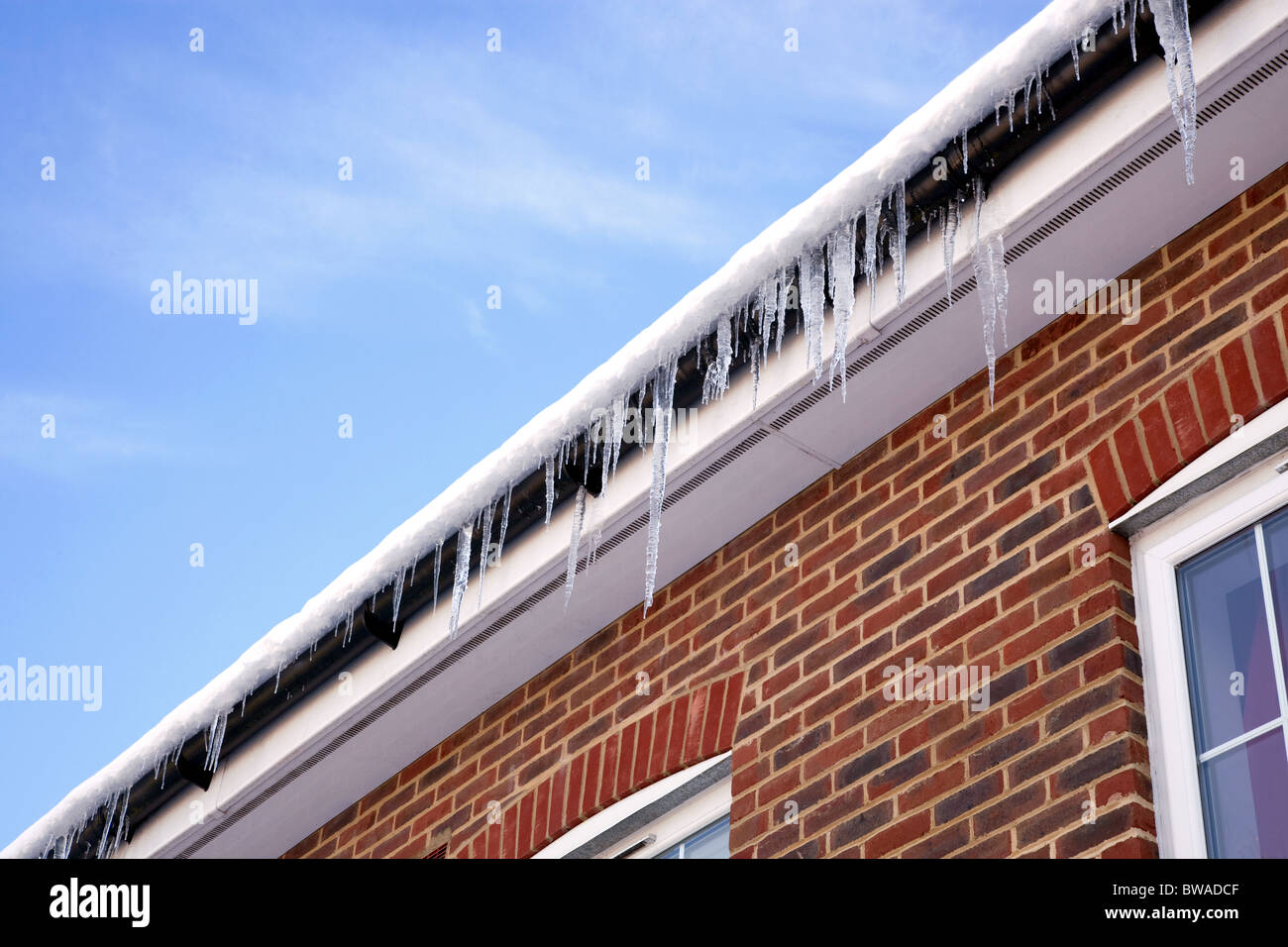 Immagine invernale di ghiaccioli appesi da grondaia sulla coperta di neve tetto di una casa moderna. Foto Stock