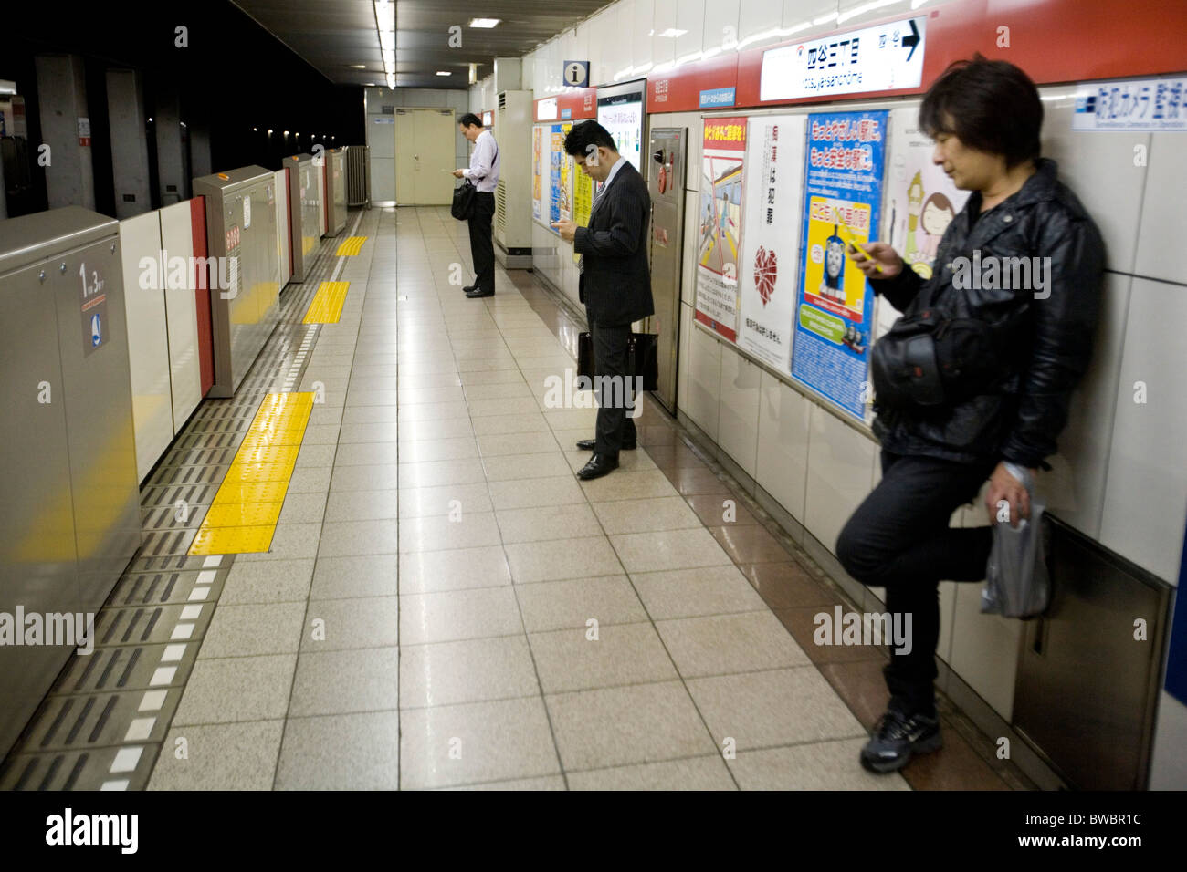 Le persone che usano il telefono cellulare mentre si è in attesa per la trainn alla piattaforma della metropolitana, Tokyo, Giappone. Foto Stock