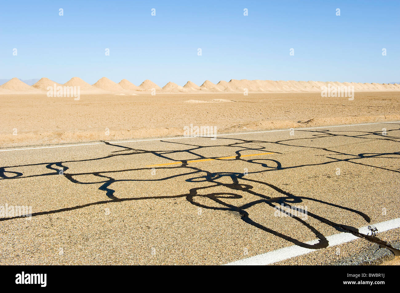 Strada con design di catrame sulla periferia di Amboy, California, con le saline e tumuli in distanza. Foto Stock
